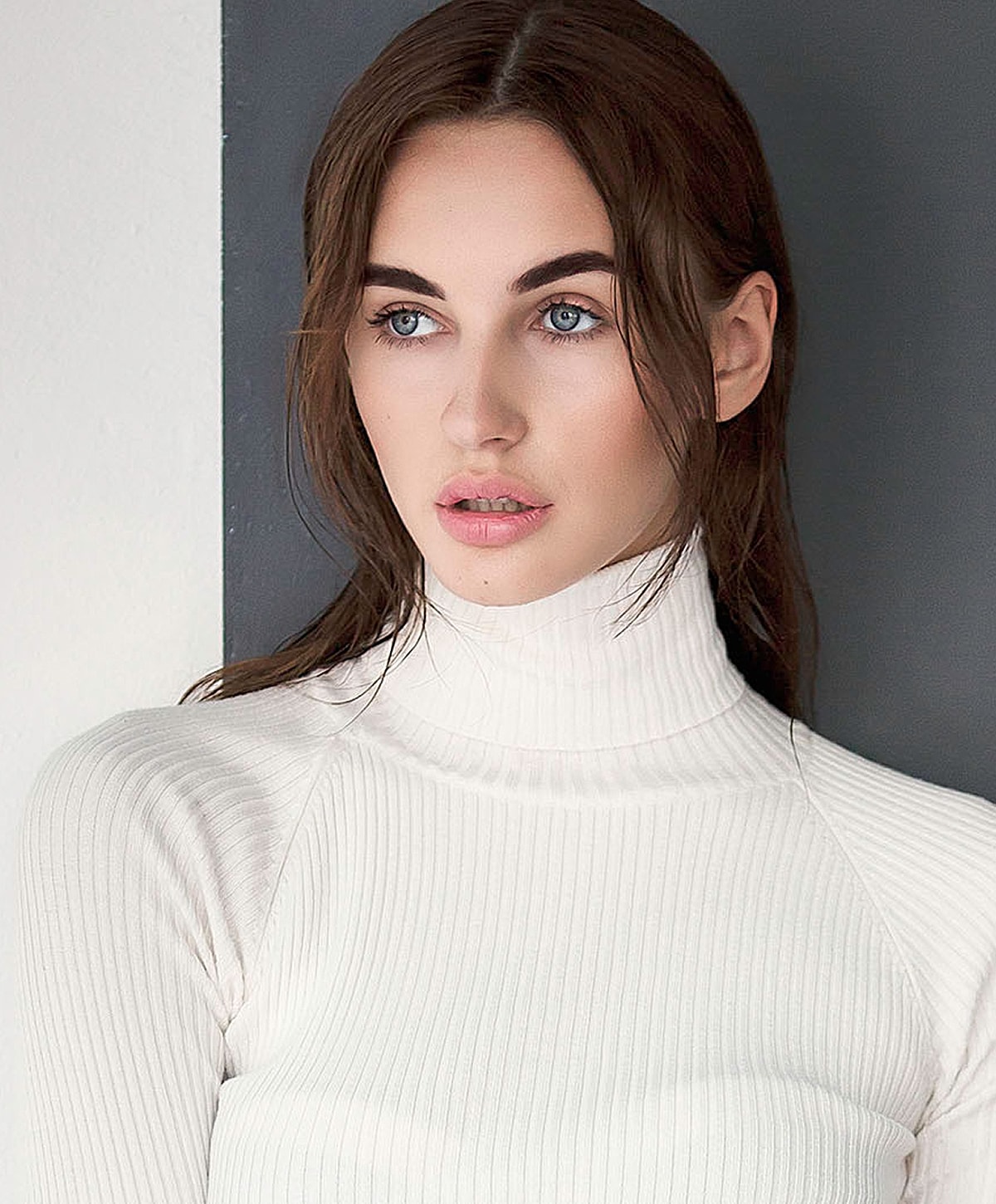 Model in white turtleneck against dark background.
