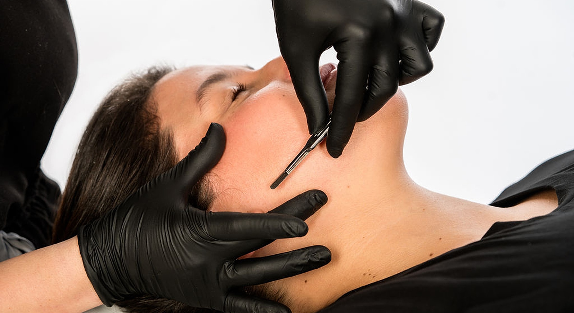 Facial treatment with tools and gloved hands.