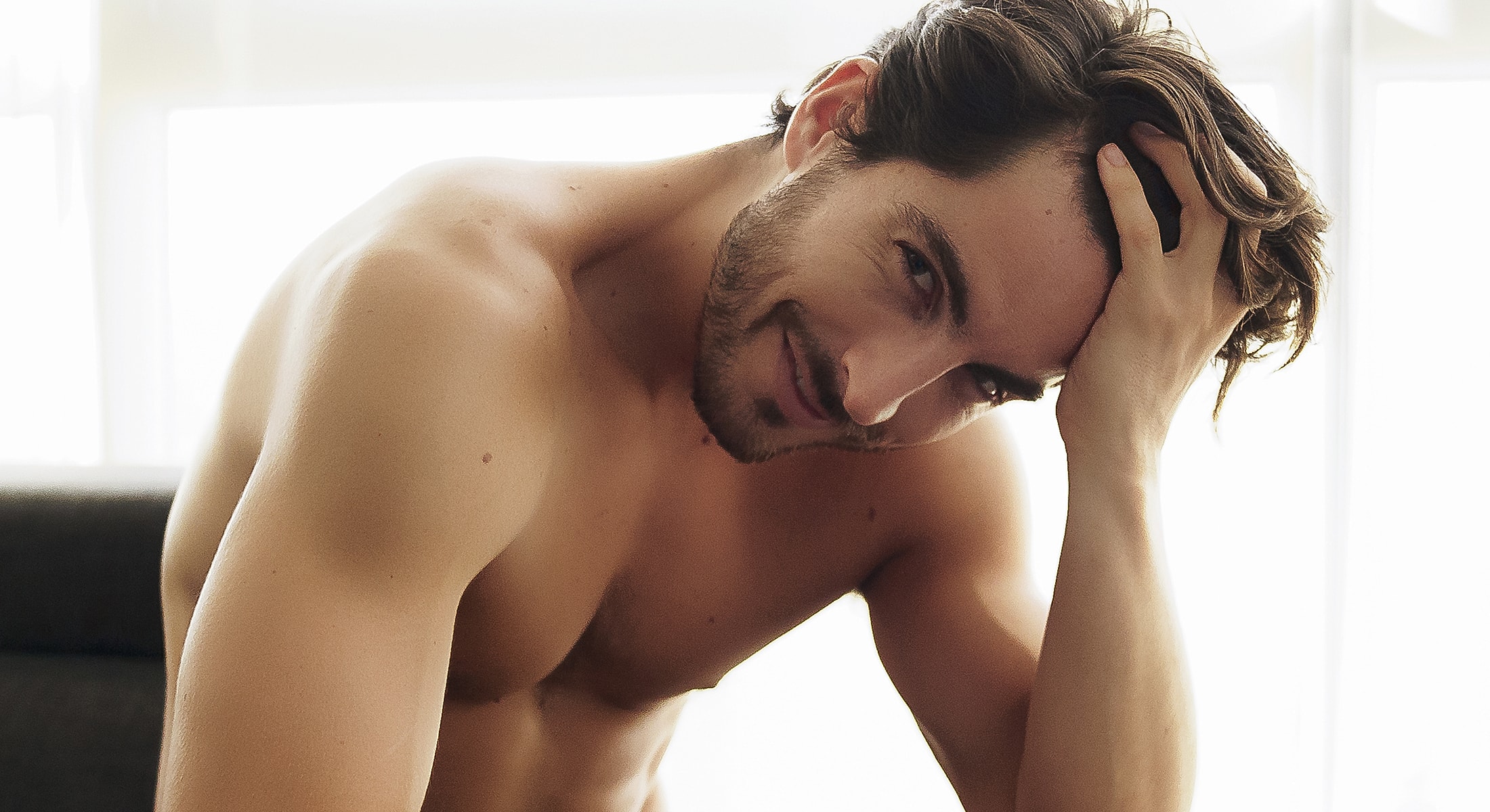 Man smiling flirtatiously with tousled hair.