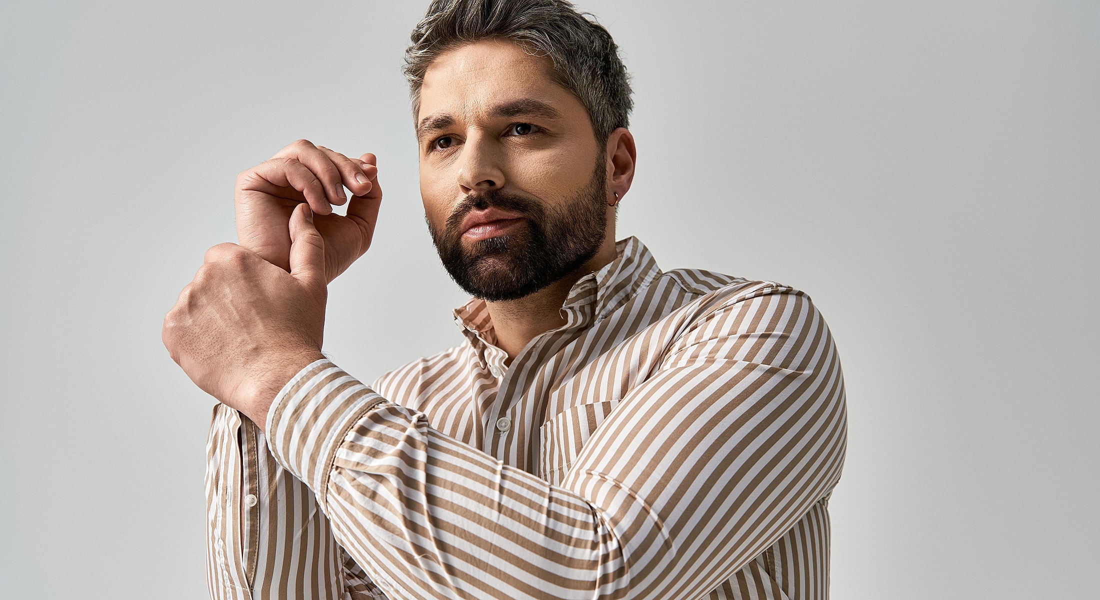 Man adjusting his shirt, thoughtful expression, studio background.