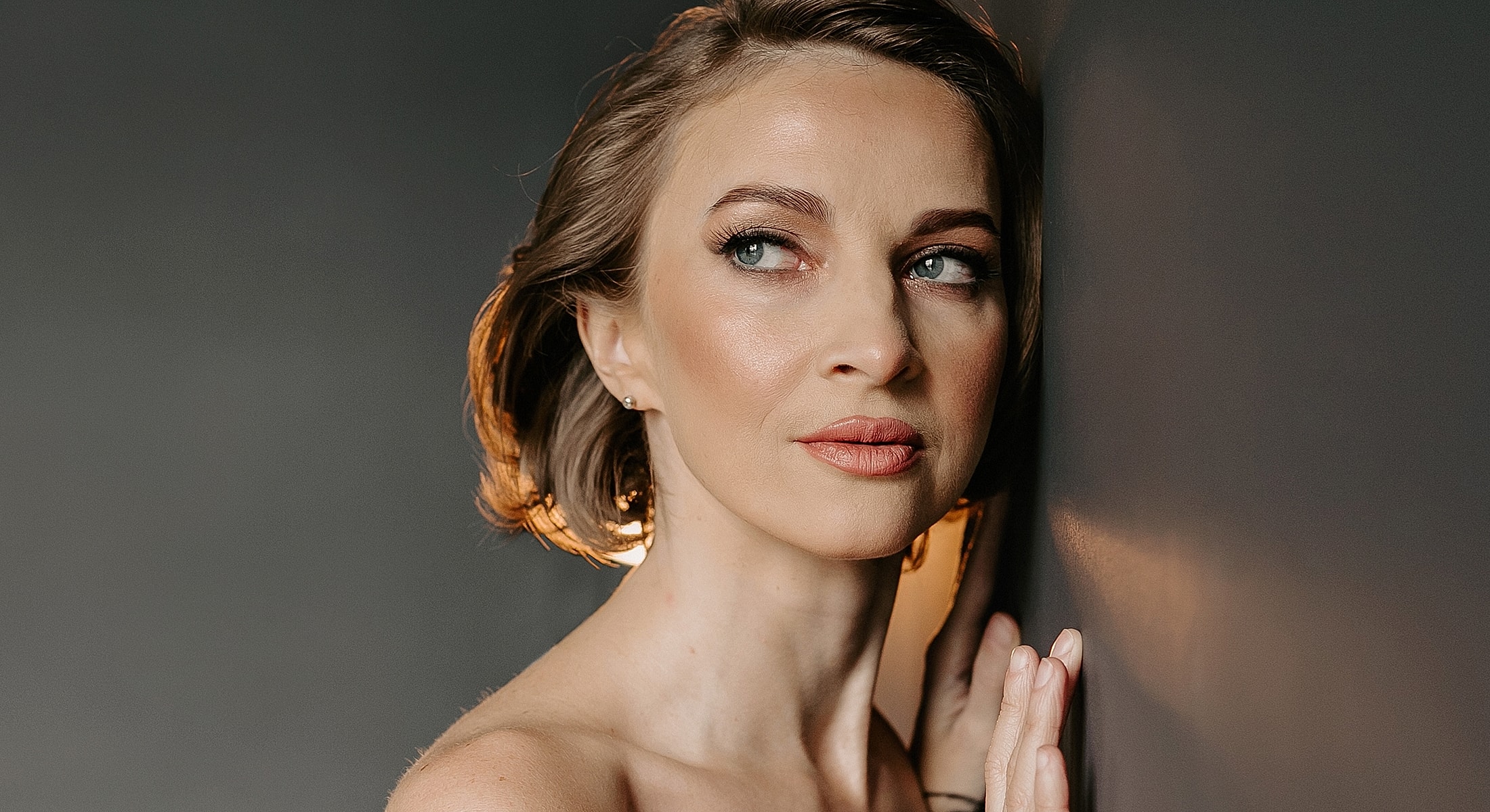 Woman posing elegantly against a dark wall.